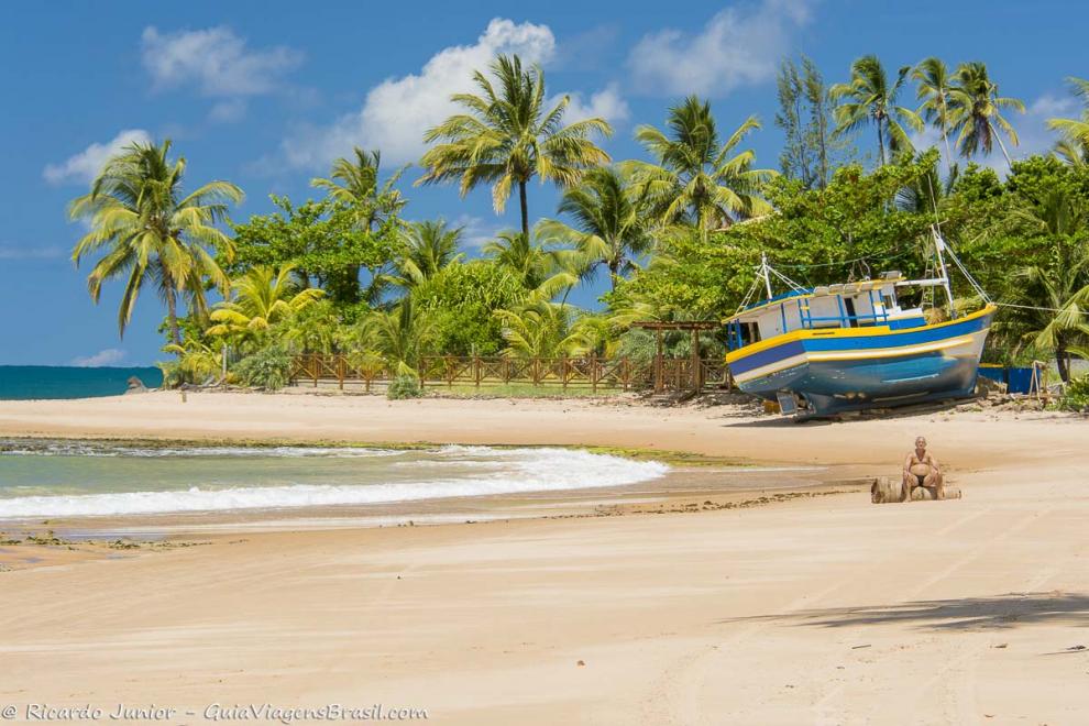 Imagem de um barco na areia e um senhor sentado contemplando o magnífico visual.